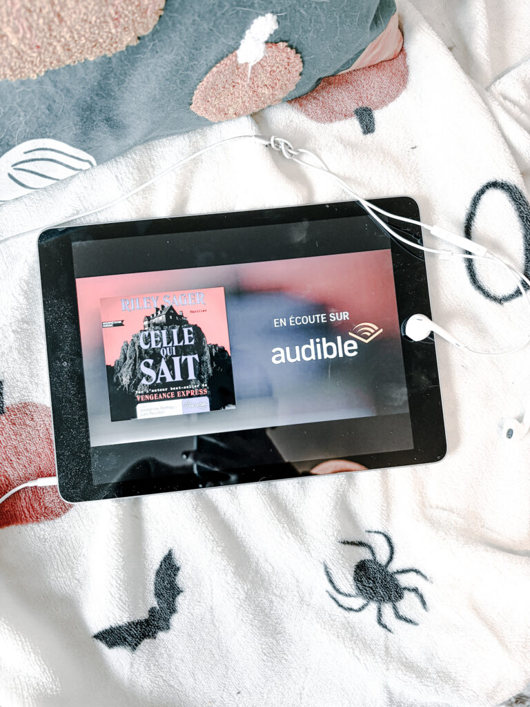iPad qui affiche Celle qui sait de Riley Sager en écoute chez Audible posé sur un canapé avec un plaid action à citrouilles et araignées