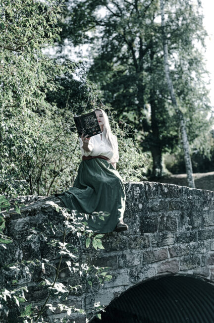 Femme assise sur un pont en pierre avec L'âtre enchanté de Delemhach dans le parc des remparts de Wissembourg.