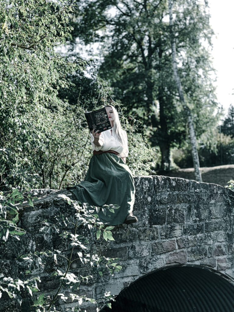 Femme assise sur un pont en pierre avec L'âtre enchanté de Delemhach dans le parc des remparts de Wissembourg.