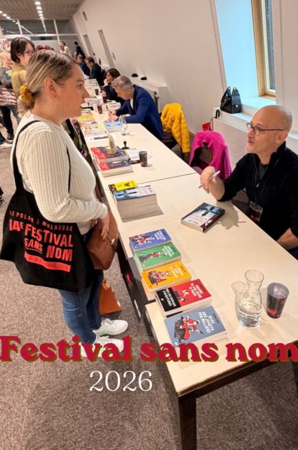 Photographie prise lors de la 14e édition du Festival Sans Nom, organisée à la bibliothèque Grand'Rue de Mulhouse en octobre 2026. On y découvre une discussion de Sorbet-Kiwi avec l'auteur Gabriel Katz, installé derrière une table de dédicaces, entouré de ses romans. D'autres auteurs et visiteurs sont visibles dans la salle. La photographie illustre l'ambiance conviviale de cette édition particulière du festival.